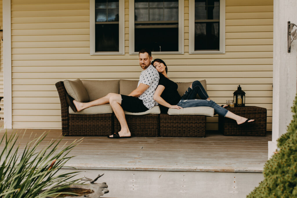 Man and woman sitting back to back looking over their shoulders at each other for in home photography session 